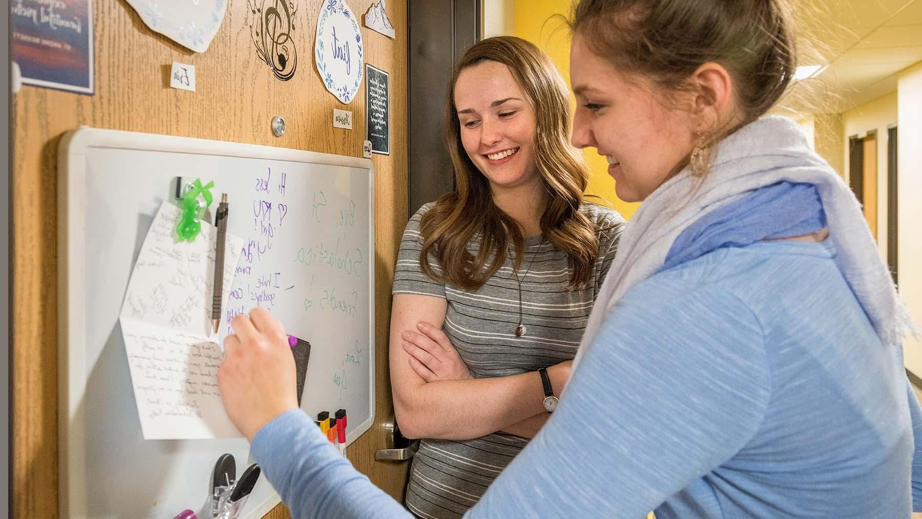两个女孩微笑着在宿舍门上的黑板上写着信息